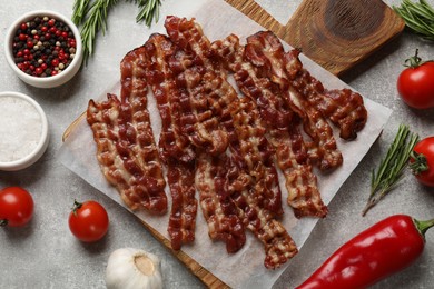 Photo of Slices of tasty fried bacon, tomatoes and different spices on light grey table, top view