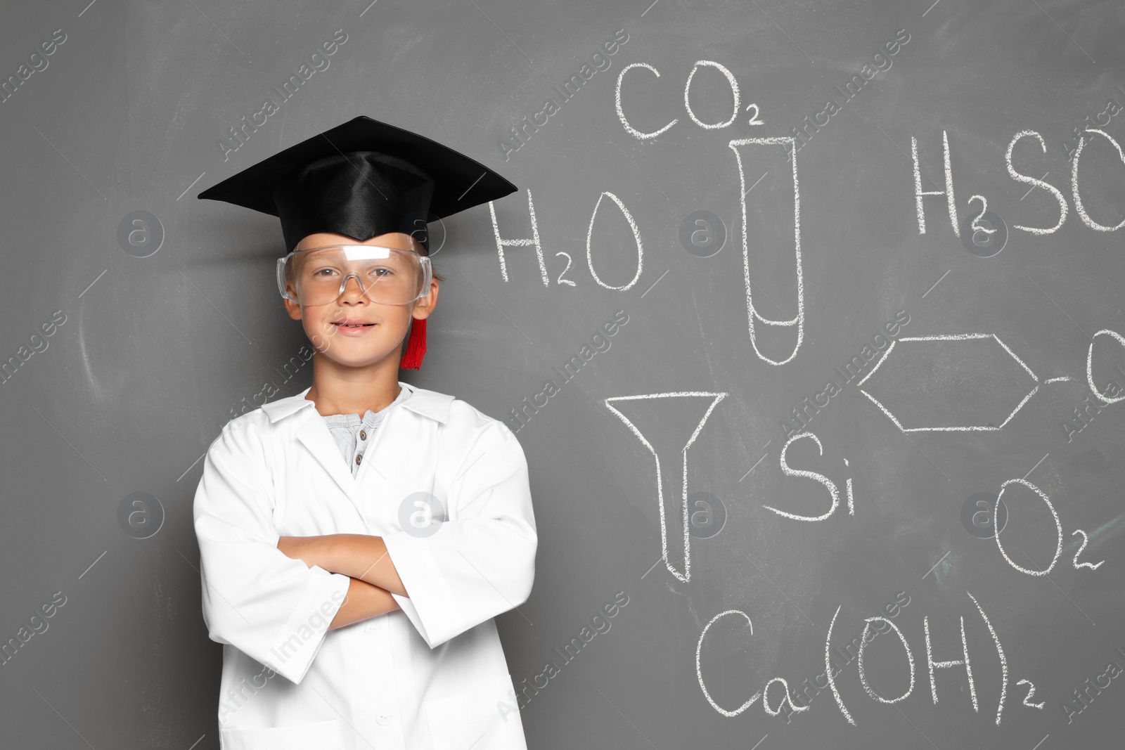 Photo of Little school child in laboratory uniform with graduate cap and chemical formulas on grey background