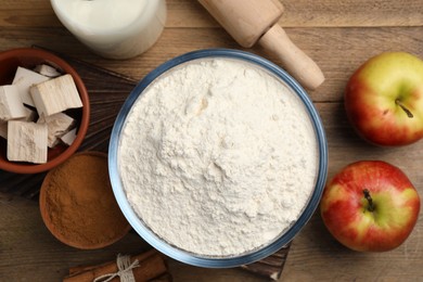 Photo of Flour, ripe apples and different ingredients on wooden table, flat lay. Cooking yeast cake