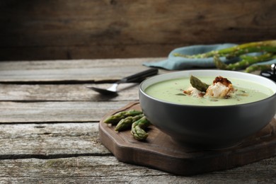 Bowl of delicious asparagus soup on wooden table, space for text