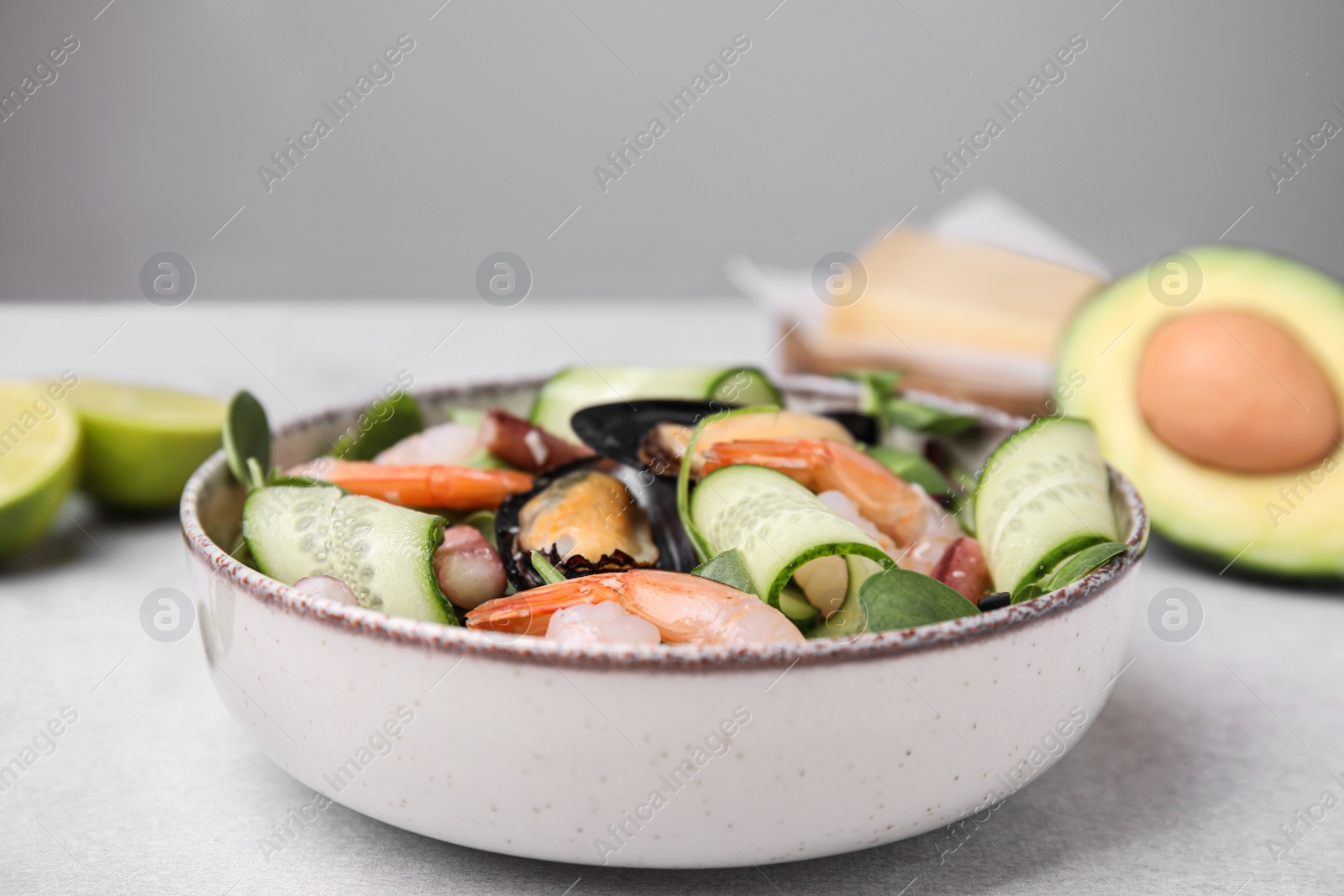 Photo of Bowl of delicious salad with seafood on light grey table