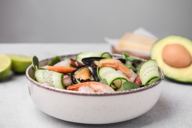 Bowl of delicious salad with seafood on light grey table