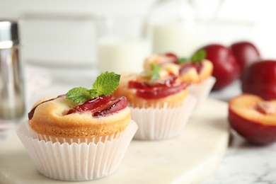 Photo of Delicious cupcakes with plums on white board, closeup