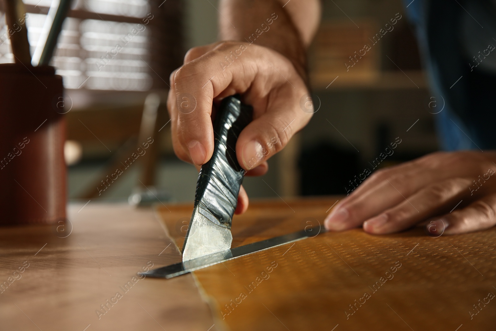 Photo of Man cutting leather with knife in workshop, closeup
