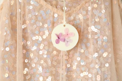 Scented sachet with flowers hanging near stylish clothes, closeup view