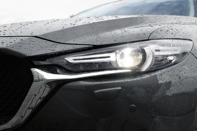 Photo of Car with switched on headlight in drops of water, closeup