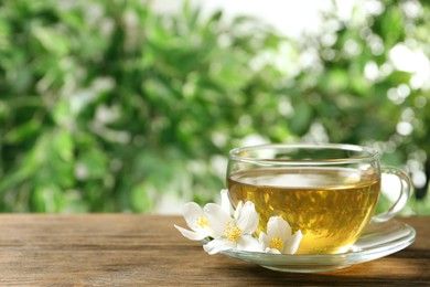 Photo of Glass cup of aromatic jasmine tea and fresh flowers on wooden table, space for text