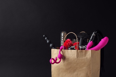 Photo of Paper shopping bag with different sex toys on black background. Space for text