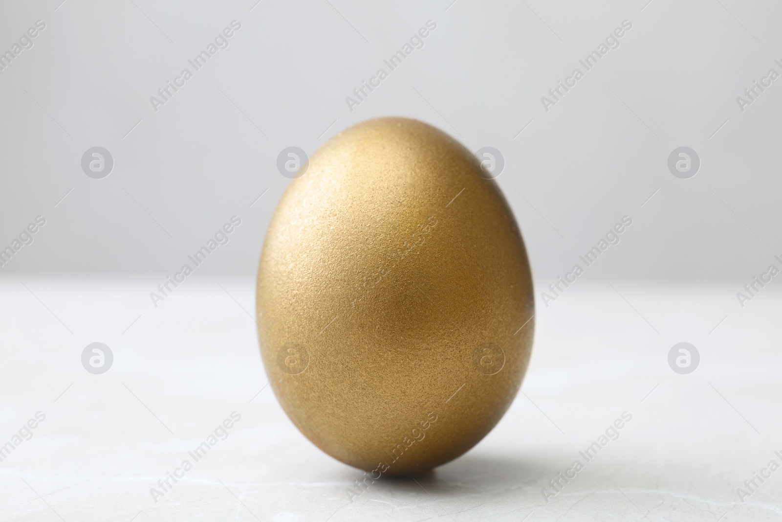 Photo of One shiny golden egg on light background