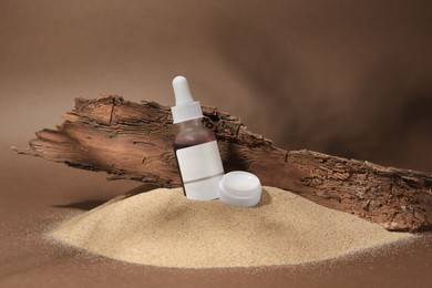Cosmetic products and tree bark on sand against brown background