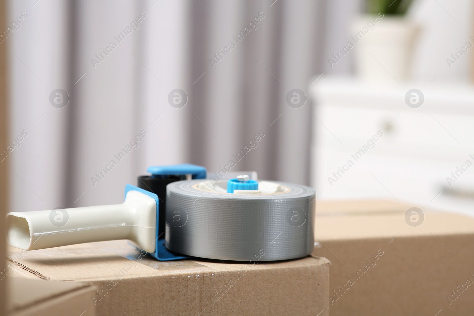 Photo of Dispenser with roll of adhesive tape on box indoors, closeup