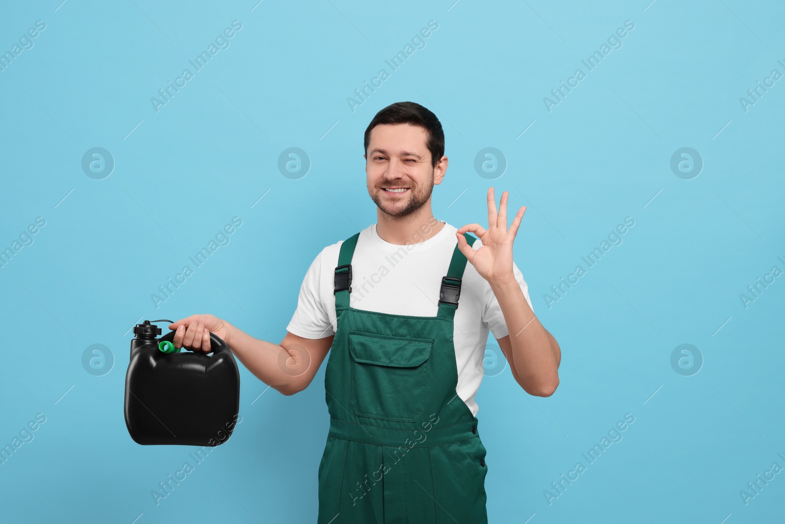 Photo of Man holding black canister and showing OK gesture on light blue background