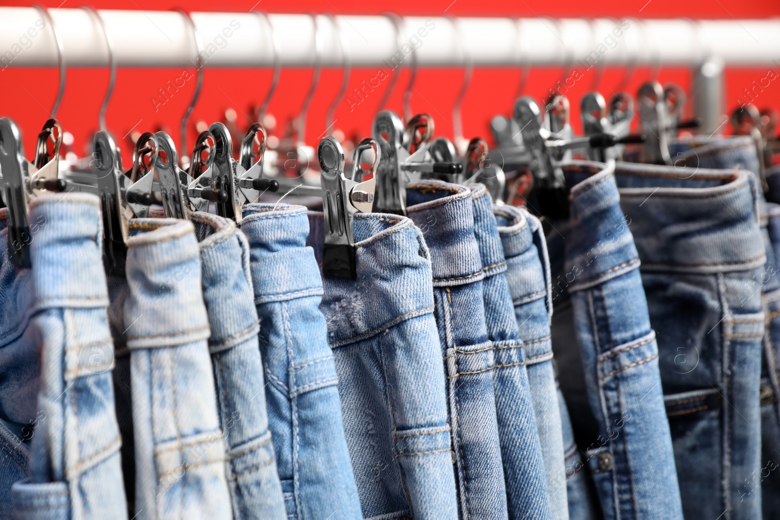 Photo of Rack with stylish jeans on red background, closeup