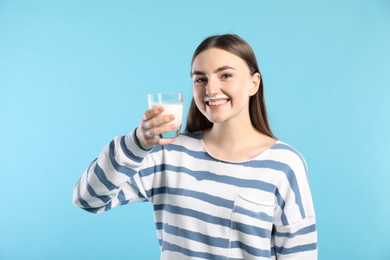 Photo of Happy woman with milk mustache holding glass of tasty dairy drink on light blue background