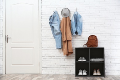 Photo of Stylish hallway interior with door, shoe rack and clothes hanging on brick wall