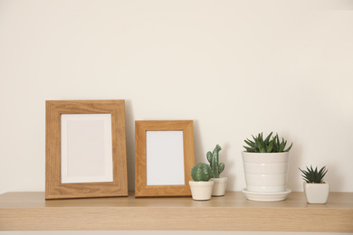 Photo of Wooden shelf with houseplants and photo frames on light wall