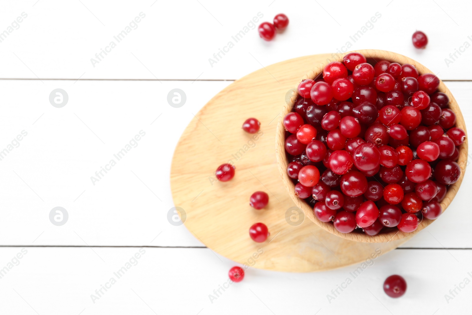 Photo of Fresh ripe cranberries in bowl on white wooden table, top view. Space for text