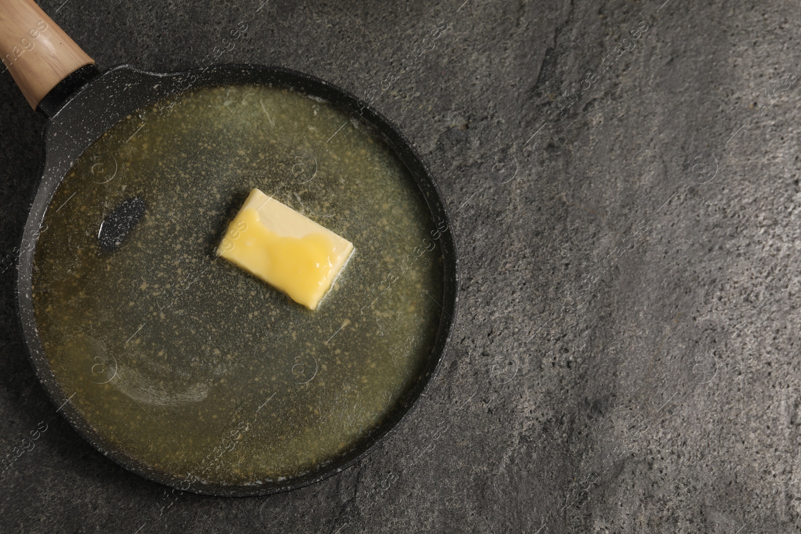 Photo of Melting butter in frying pan on grey table, top view. Space for text