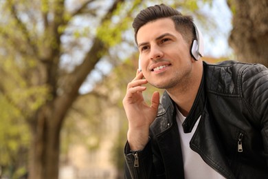 Photo of Handsome man with headphones listening to music outdoors, space for text