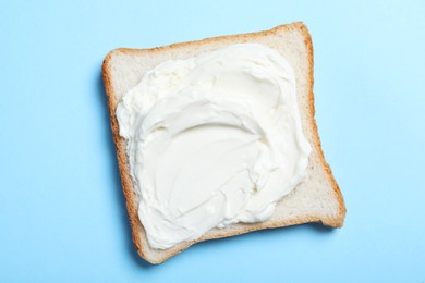 Photo of Slice of bread with tasty cream cheese on light blue background, top view