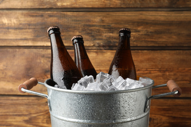 Metal bucket with beer and ice cubes on wooden background