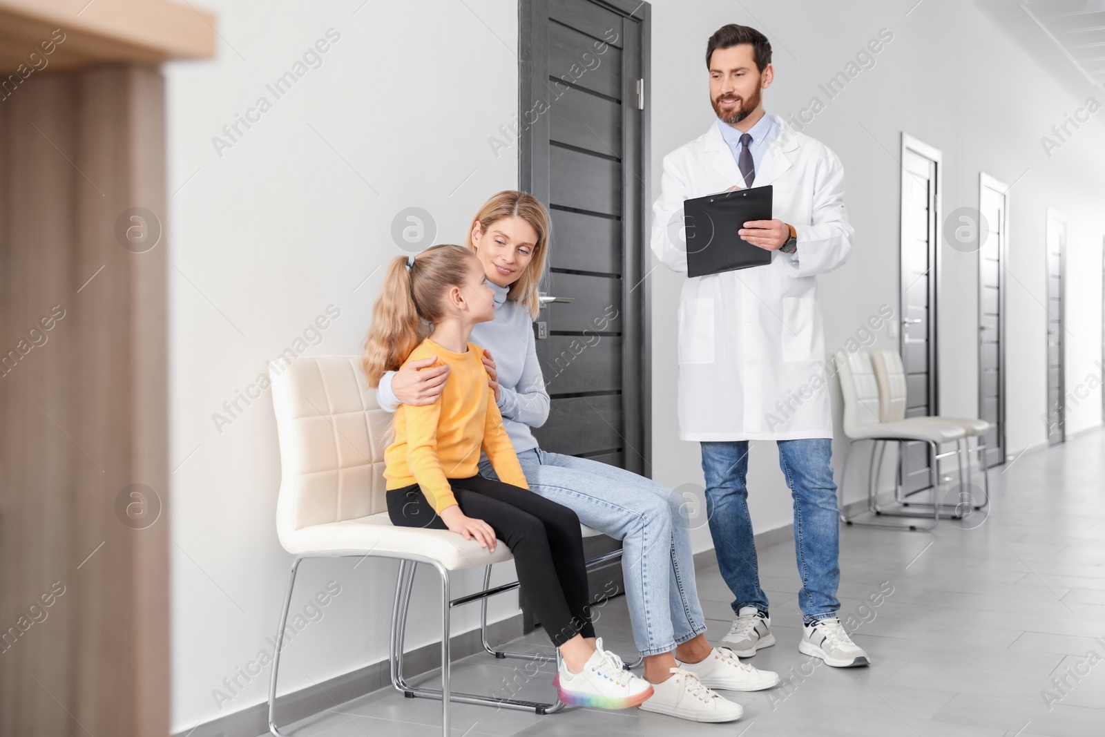 Photo of Doctor with clipboard consulting mother and daughter in clinic