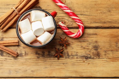 Photo of Tasty hot chocolate with marshmallows, candy cane and spices on wooden table, flat lay. Space for text