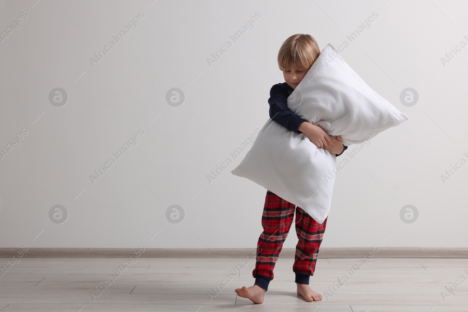 Photo of Little boy hugging pillow indoors, space for text