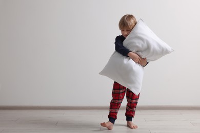 Photo of Little boy hugging pillow indoors, space for text