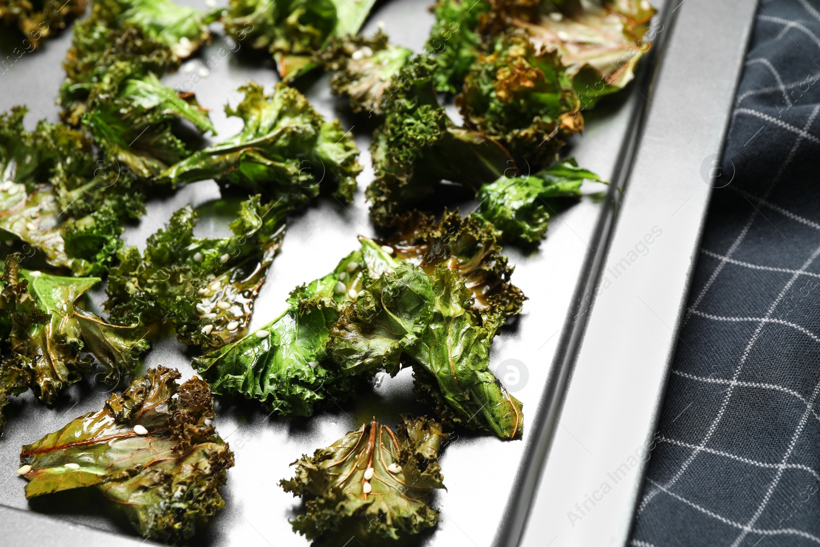 Photo of Tasty kale chips with seeds on baking sheet, closeup