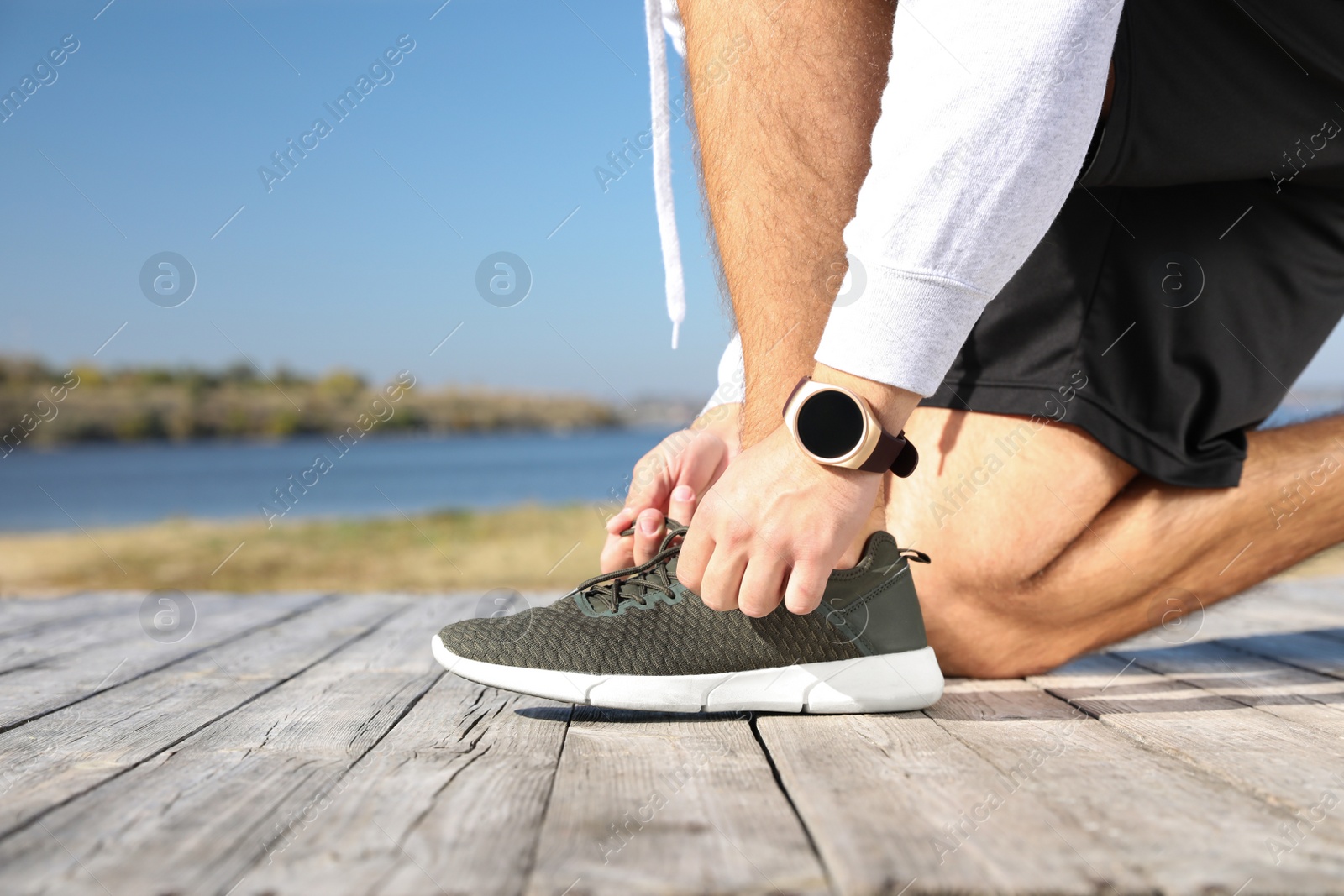 Image of Sporty man tying shoelaces near river on sunny morning, closeup