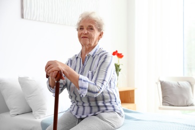 Photo of Elderly woman with walking cane sitting on bed in nursing home. Medical assistance