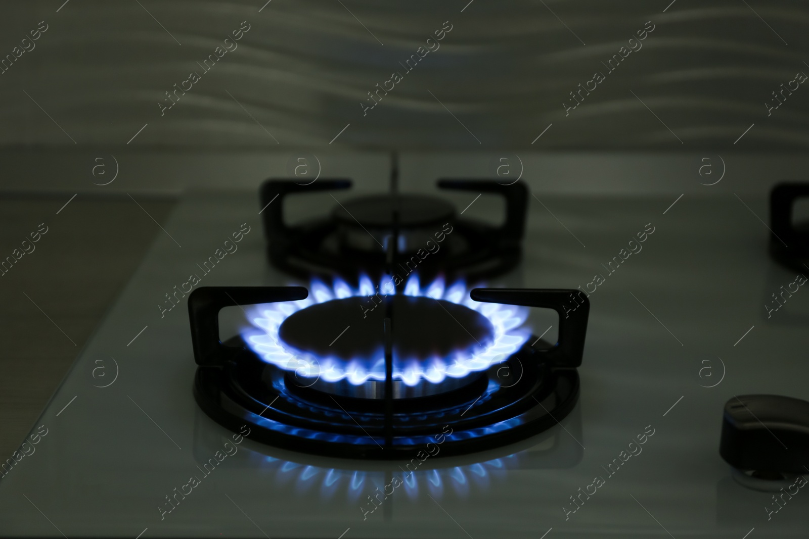 Photo of Modern gas cooktop with burning blue flame in kitchen at night