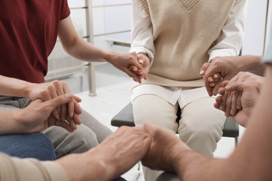 Photo of Psychotherapist and group of drug addicted people holding hands together at therapy session, closeup