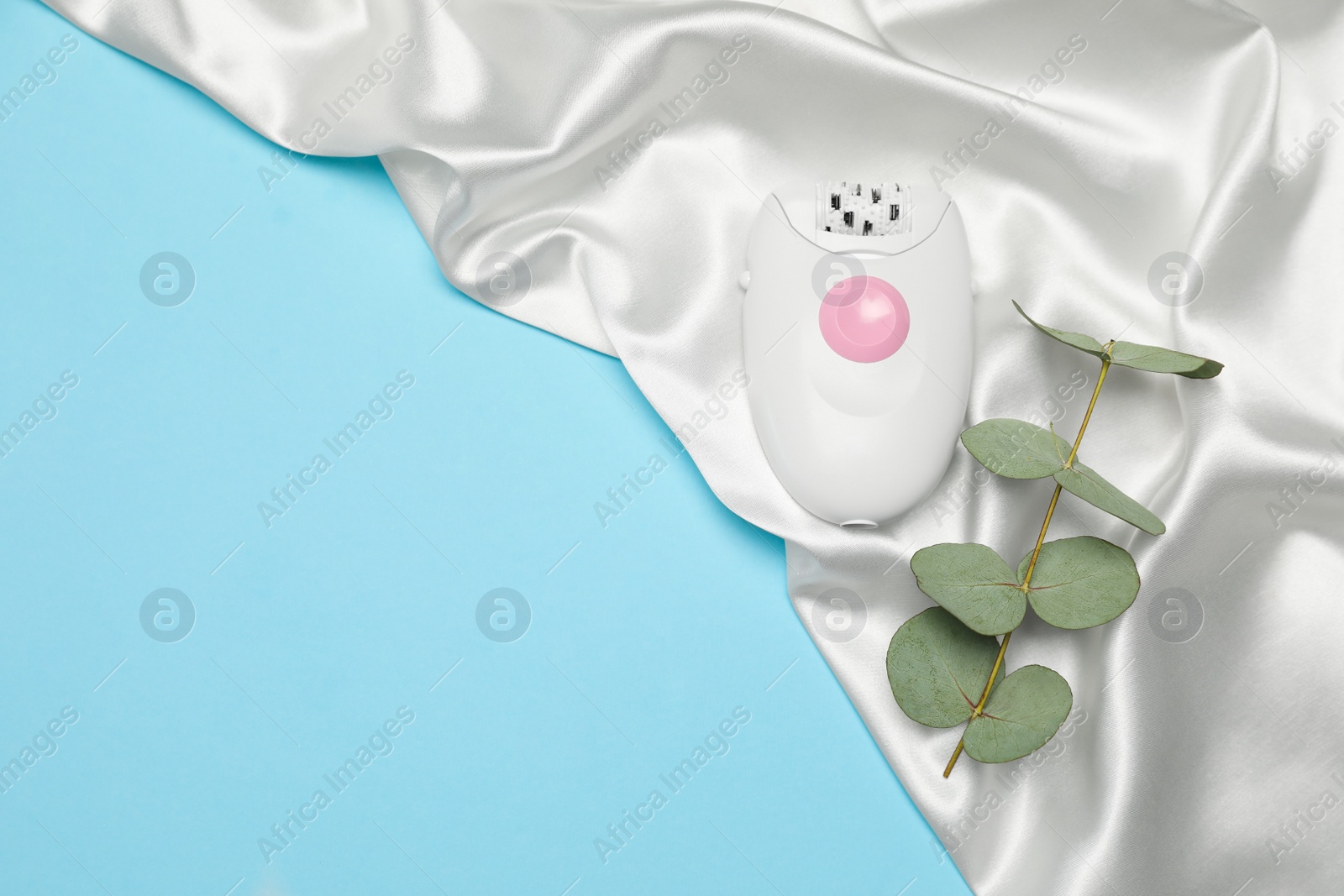Photo of Epilator, eucalyptus and white silk fabric on light blue background, flat lay. Space for text