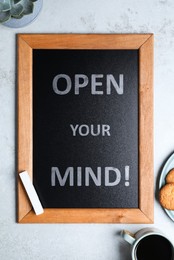 Small chalkboard with motivational quote Open your mind, coffee and cookies on light grey table, flat lay