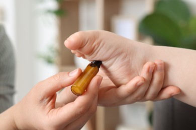 Mother applying essential oil from roller bottle onto her baby`s heel indoors, closeup