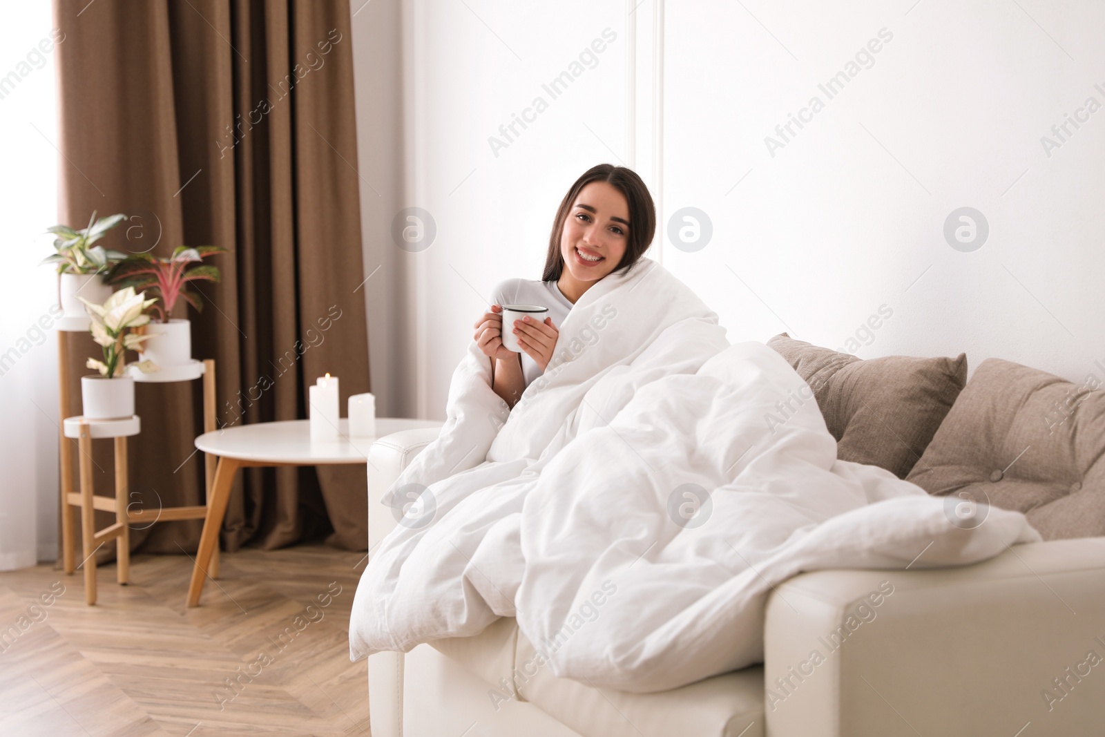 Photo of Woman covered in blanket holding cup of drink on sofa