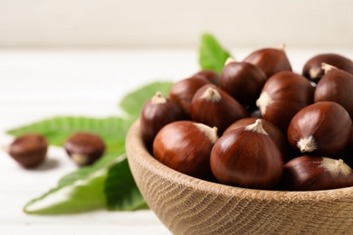 Photo of Fresh sweet edible chestnuts in bowl on white table, closeup
