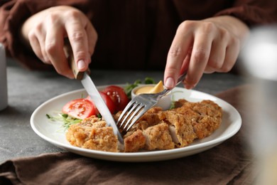 Photo of Woman eating delicious schnitzel at grey table, closeup
