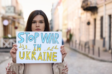 Photo of Sad woman holding poster Stop War in Ukraine on city street. Space for text