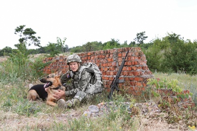 Man in military uniform with German shepherd dog near broken brick wall