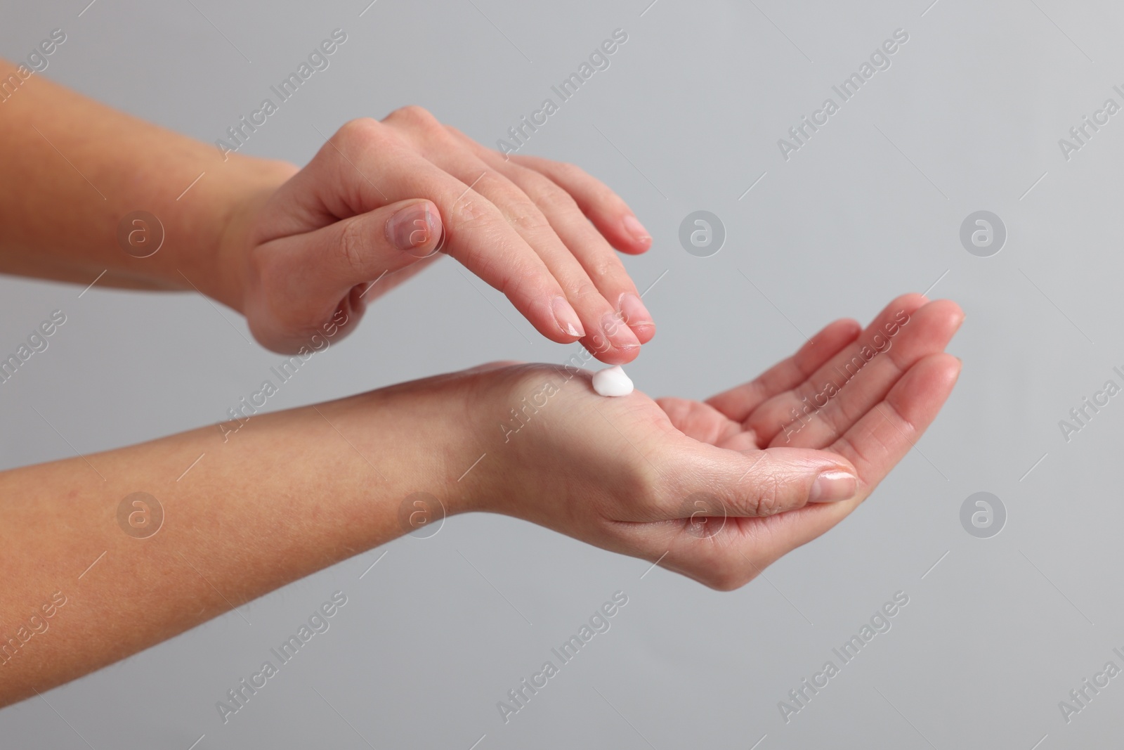 Photo of Woman applying cosmetic cream onto hand on light grey background, closeup