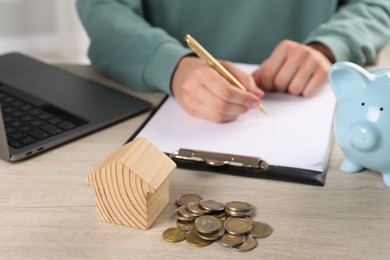 Photo of Woman planning budget at wooden table, focus on house model and coins