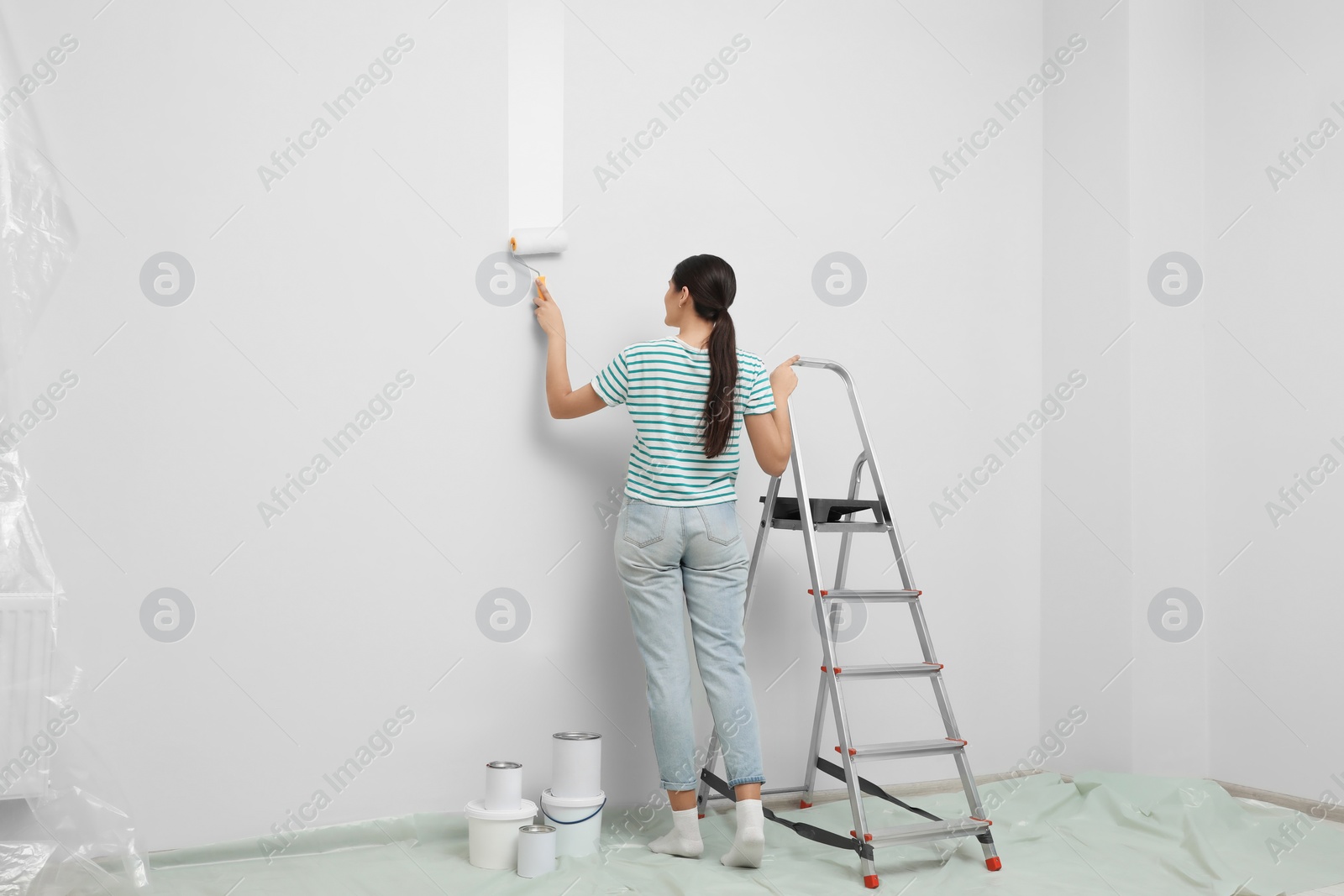 Photo of Woman near metallic folding ladder and painting wall indoors, back view