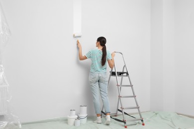 Photo of Woman near metallic folding ladder and painting wall indoors, back view