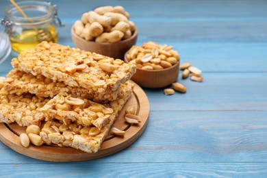 Photo of Delicious peanut bars (kozinaki) and ingredients on light blue wooden table. Space for text
