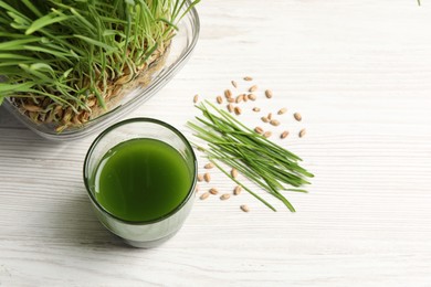 Wheat grass drink in glass, seeds and fresh green sprouts on white wooden table, flat lay