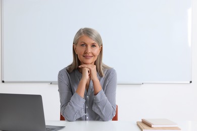 Happy professor sitting near laptop at desk in classroom, space for text