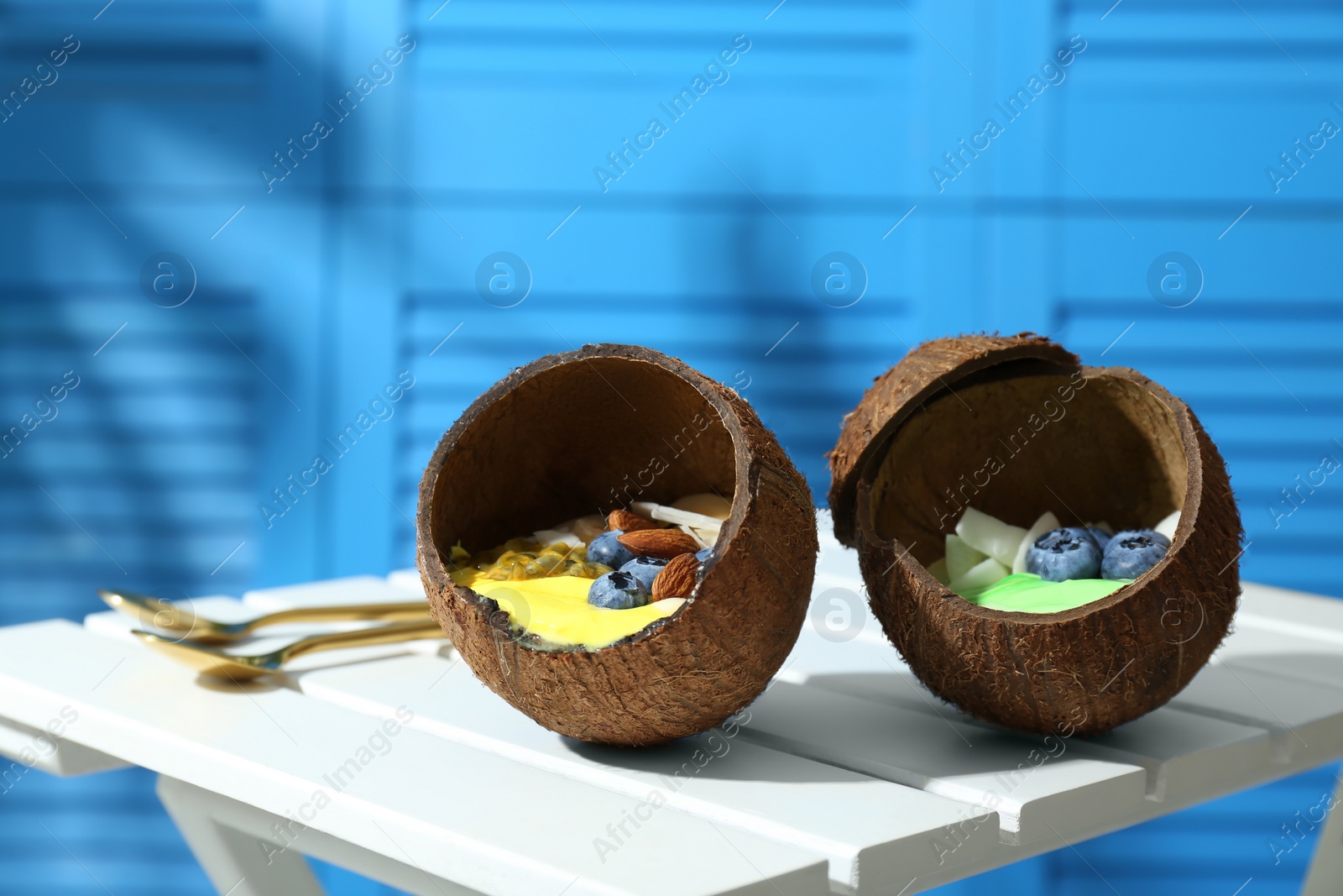 Photo of Tasty smoothie bowl served in coconut shells on white wooden table